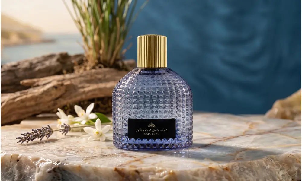 Blue textured Bois Bleu perfume bottle with a gold cap, set on marble with lavender and driftwood.