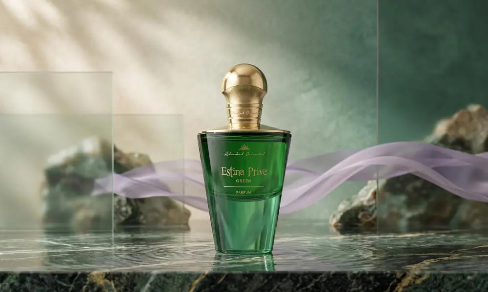 Green Estina Prive bottle on dark marble, with rocks, glass, and purple ribbons against a texture-walled backdrop.