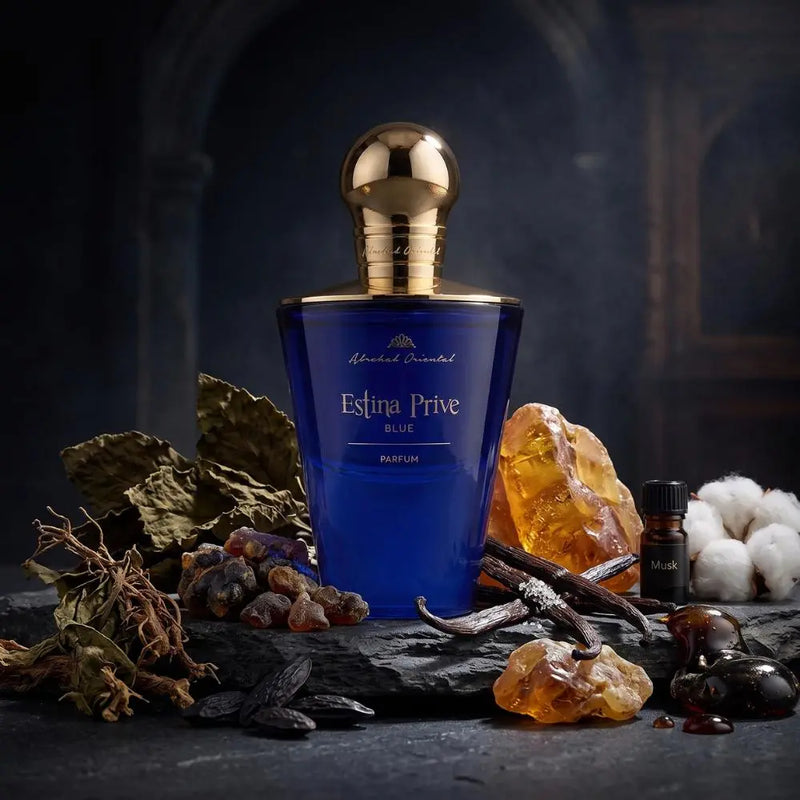 A blue perfume bottle with a gold cap labeled 'Abelred Oriental Eslina Prive BLADE' is displayed on a dark stone surface with dried botanicals, amber crystals, vanilla pods, and cotton against a dark moody background.