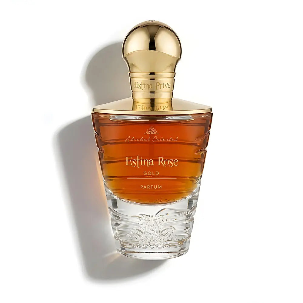 A bottle of Estina Rose Gold Parfum by Mariah's Essential, featuring an amber-colored liquid in a clear glass bottle with a shiny gold cap, set against a plain white background with a soft shadow.