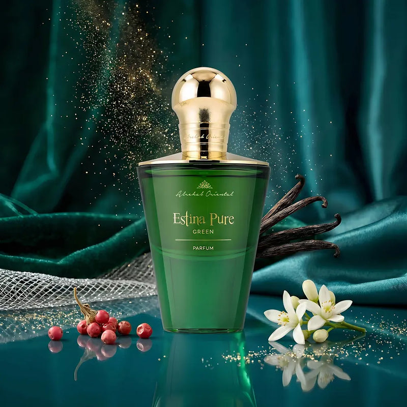 A green perfume bottle with a shiny gold cap, labeled 'Almari Estina Pure GREEN PARFUM', set against a draped teal fabric background with decorative flowers, vanilla pods, and gold glitter.