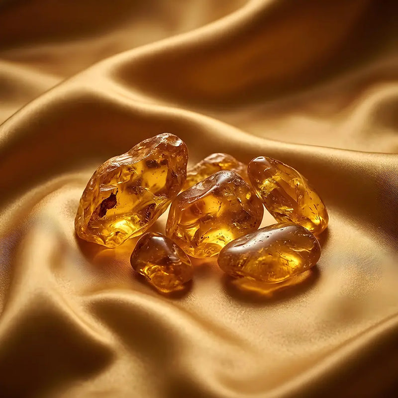 Five polished amber-yellow translucent stones arranged on draped satin fabric with a warm golden glow.
