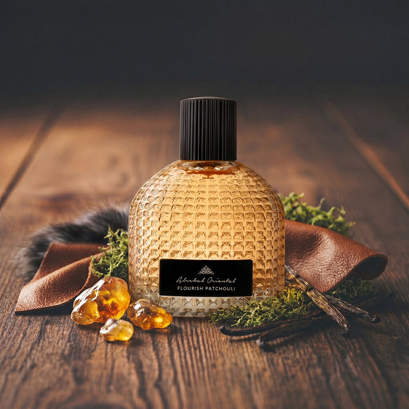 A textured glass perfume bottle filled with amber liquid, featuring a black ribbed cap and a black label that reads 'Alcohol Free Flavour Patchouli.' It is styled on a rustic wooden surface with brown leather, green moss, vanilla beans, and amber crystals.