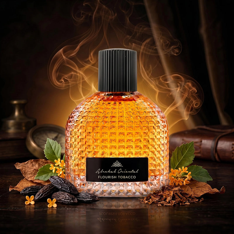 A textured glass perfume bottle filled with amber liquid, labeled 'Ahmad Olayil Flourish Tobacco,' set on a dark wooden surface with dried tobacco leaves, small yellow flowers, and smoky orange vapor in a moody, warm-toned scene.