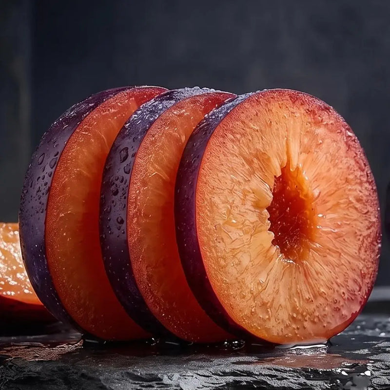 Four sliced plums with deep purple skins and bright orange-red flesh, arranged upright on a dark wet surface against a dark studio background.
