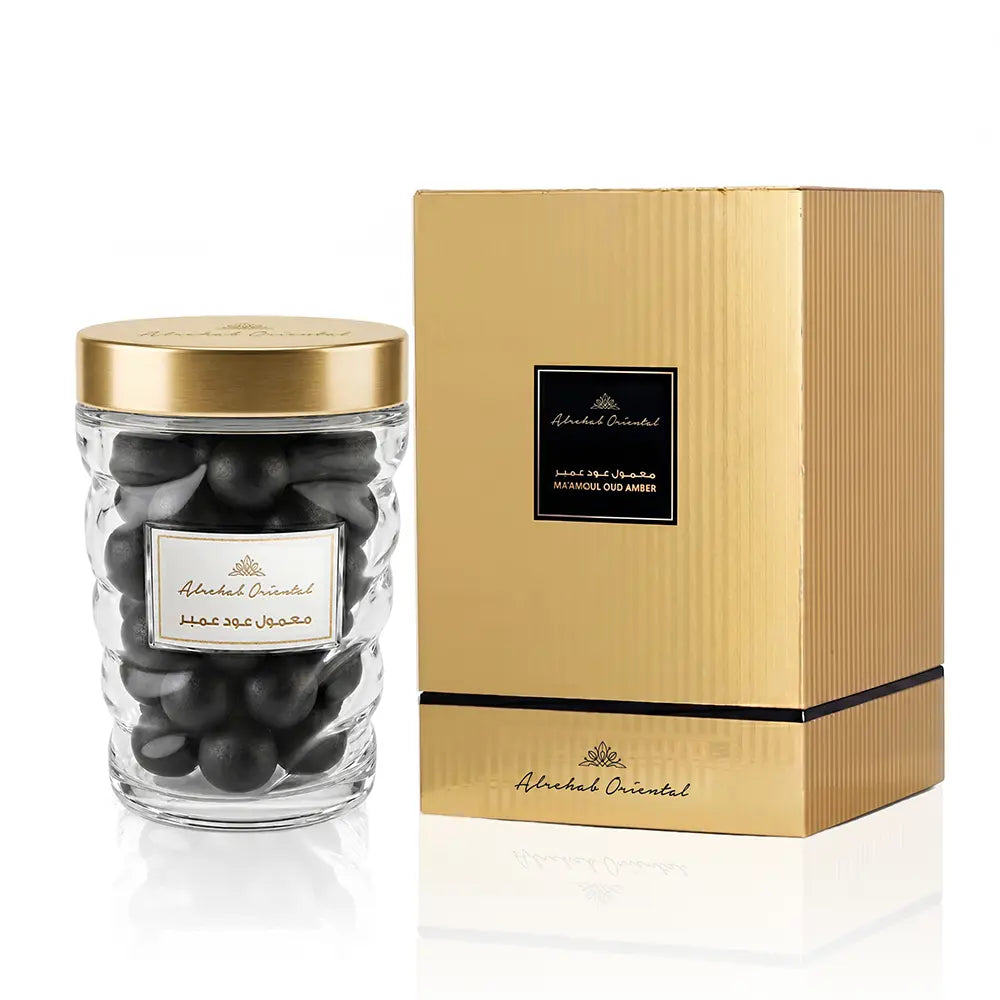 A clear glass jar filled with dark chocolate pieces, topped with a gold lid, shown next to its textured gold packaging box. Both items feature a black label with the brand name 'Abdel Oriental'.