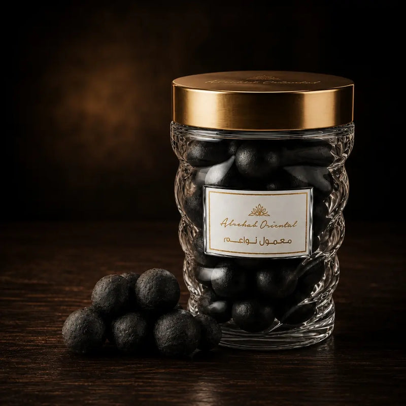 A clear glass jar filled with Maamoul, topped with a metallic gold lid, set on a dark wooden surface