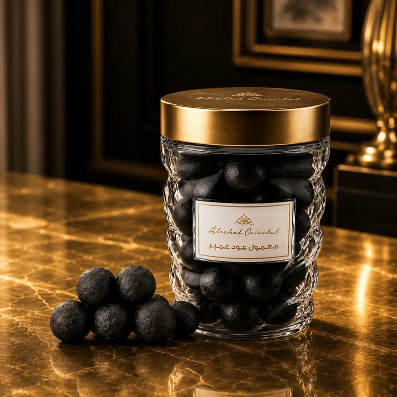 A clear textured glass jar filled with Maamoul, topped with a shiny gold lid , set on a reflective gold marble surface.