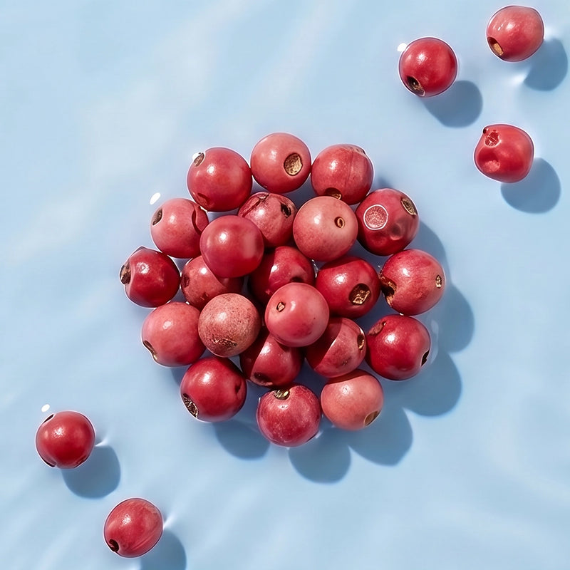 A pile of glossy, round cranberry-like red beads with small holes, scattered on a light blue textured background.